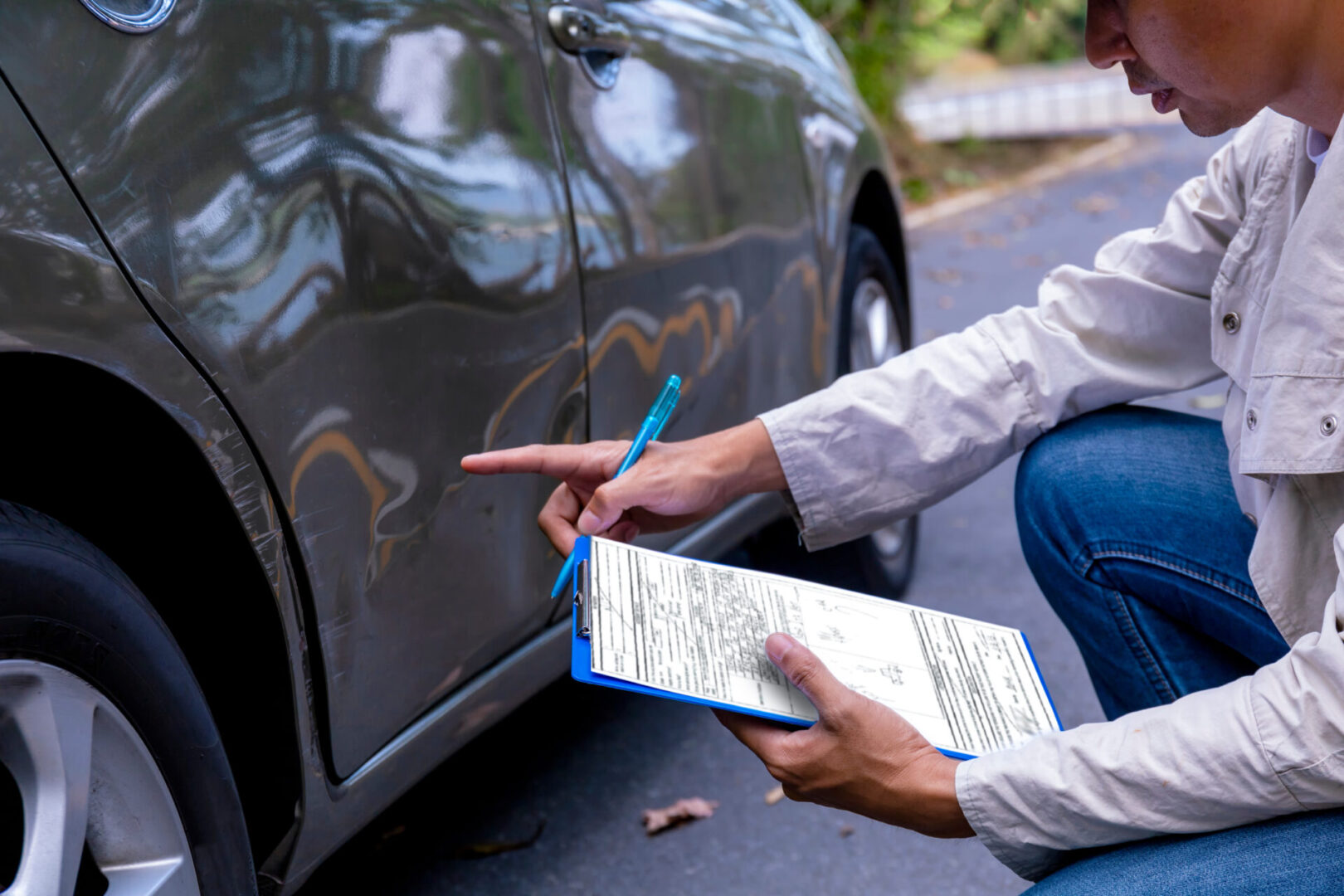 Insurance agent writing on clipboard while examining car after